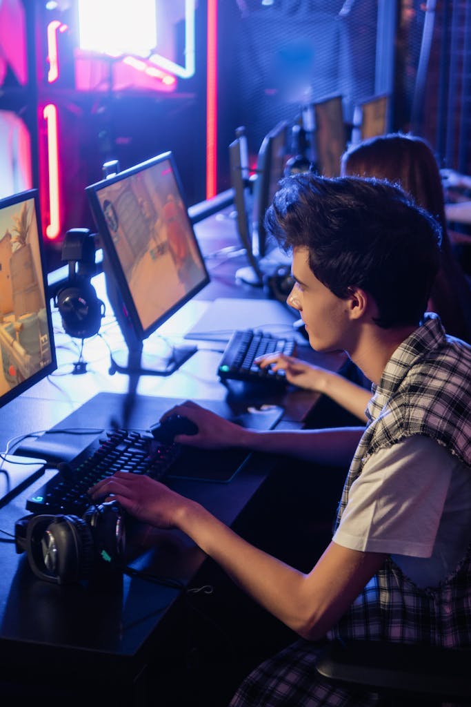 Two teenagers playing video games on computers in an esports arena setting.