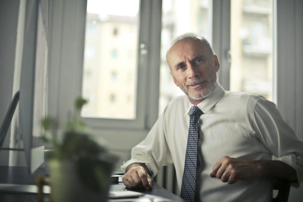 A mature man in professional attire smiling in an office setting.